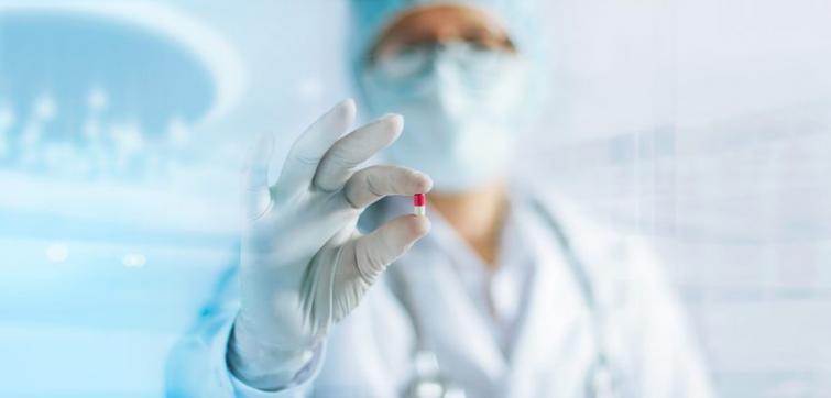 Person in a lab coat and a mask holding a pill