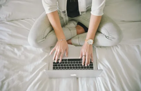 Student sitting on bed typing on laptop